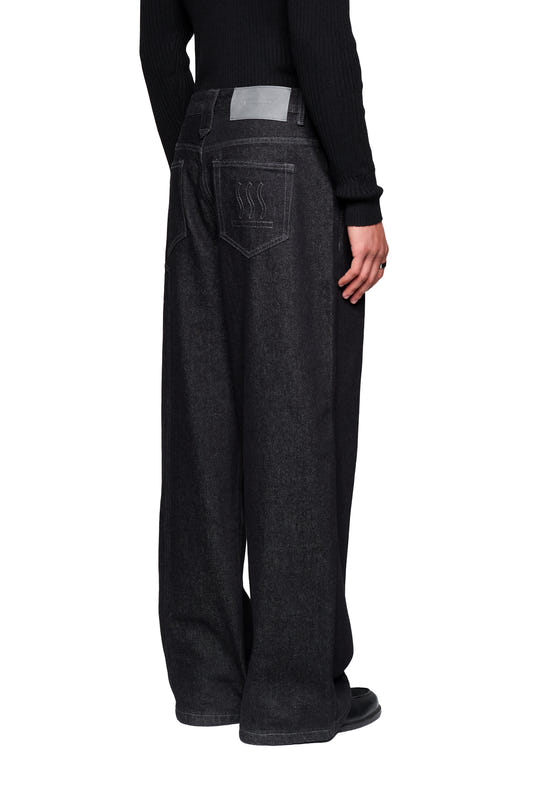 Rückansicht der Raw Denim Pants Black mit weiten Beinen, Patch-Taschen und dezenter Stickerei, getragen mit schwarzem Oberteil und Schuhen.