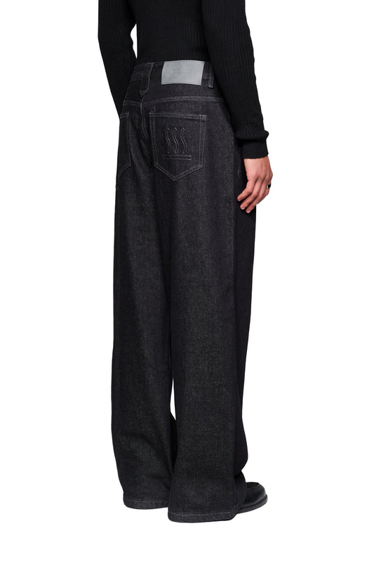 Rückansicht der Raw Denim Pants Black mit weiten Beinen, Patch-Taschen und dezenter Stickerei, getragen mit schwarzem Oberteil und Schuhen.