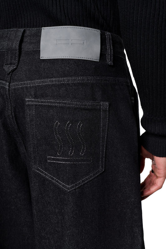 Rückansicht der Raw Denim Pants Black mit dekorativer Stickerei auf der Gesäßtasche und grauem PU-Patch am Bund, kombiniert mit einem schwarzen Pullover.