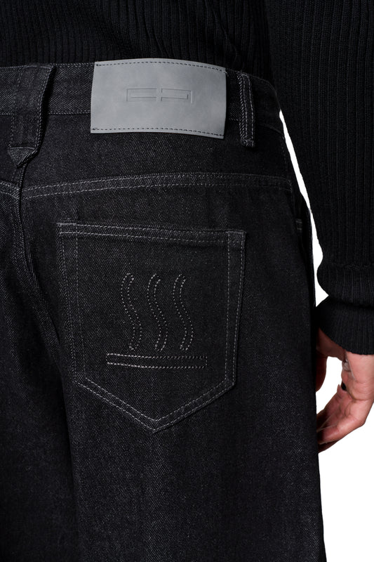 Rückansicht der Raw Denim Pants Black mit dekorativer Stickerei auf der Gesäßtasche und grauem PU-Patch am Bund, kombiniert mit einem schwarzen Pullover.