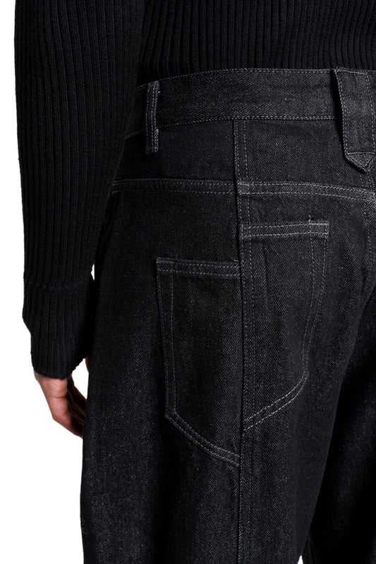 Rückansicht der Raw Denim Pants Black: schwarze Jeans mit Gesäßtaschen, Gürtelschlaufen und markanten Nähten, kombiniert mit einem schwarzen Strickpullover.