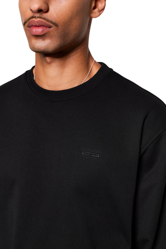 Mann trägt Mokka Sweater mit dezentem Brustdetail und silberner Halskette. Perfekt für Alltag, inspiriert vom CC Core Hoodie für optimalen Komfort.