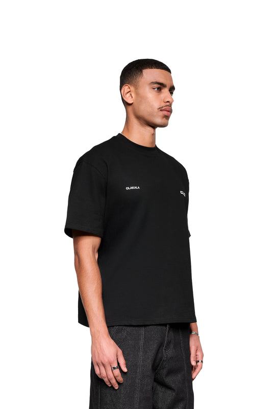 Ein junger Mann trägt das Mokka T-Shirt Black mit lockerem Schnitt und kleinem OLAKALA-Logo links auf der Brust, ergänzt durch silberne Ringe.