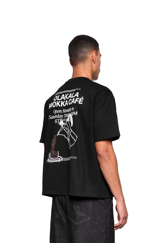 Rückansicht des Mokka T-Shirt Black mit großem OLAKALA MOKKA CAFÉ-Print und Mokkakanne-Motiv, getragen von einem Model in dunkler Jeans.