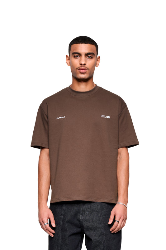 Junger Mann trägt das Mokka T-Shirt Brown im boxy-Fit mit dezentem OLAKALA-Logo und großem Rückendruck, kombiniert mit dunklen Jeans.