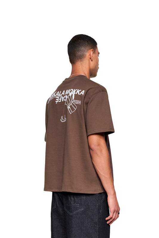 Rückansicht des Mokka T-Shirts Braun mit großem Print “MOKKA” und Moka-Kanne, getragen von einem Mann in Jeans. Boxy, oversized Fit von OLAKALA.