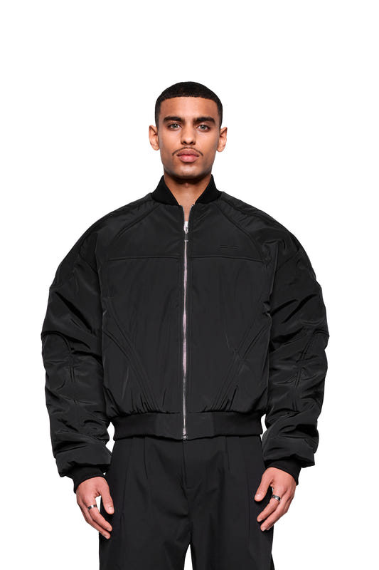 A young man is wearing the Void Bomber Jacket in black, featuring a zipper, ribbed cuffs, and dynamic stitching, paired with silver rings and matching pants.