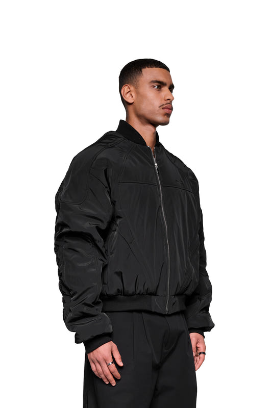 A young man wears a black Void bomber jacket with a ribbed collar and dynamic stitching, featuring pockets and a front zipper, against a white background.