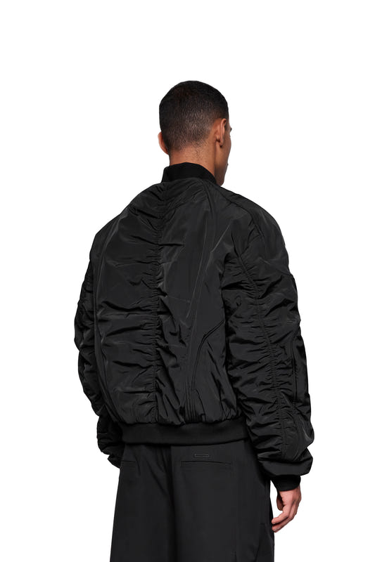 Rear view of a person wearing the Void Bomber Jacket Black, featuring slightly gathered nylon, a ribbed hem and cuffs, paired with loose-fitting black pants.