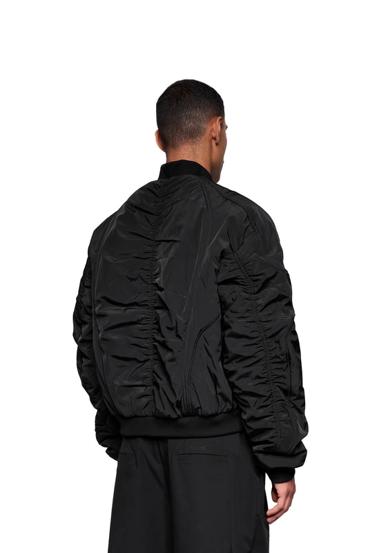 Rückansicht einer Person im Void Bomber Jacket Black mit leicht gerafftem Nylon, geripptem Saum und Bündchen, kombiniert mit lockerer schwarzer Hose.