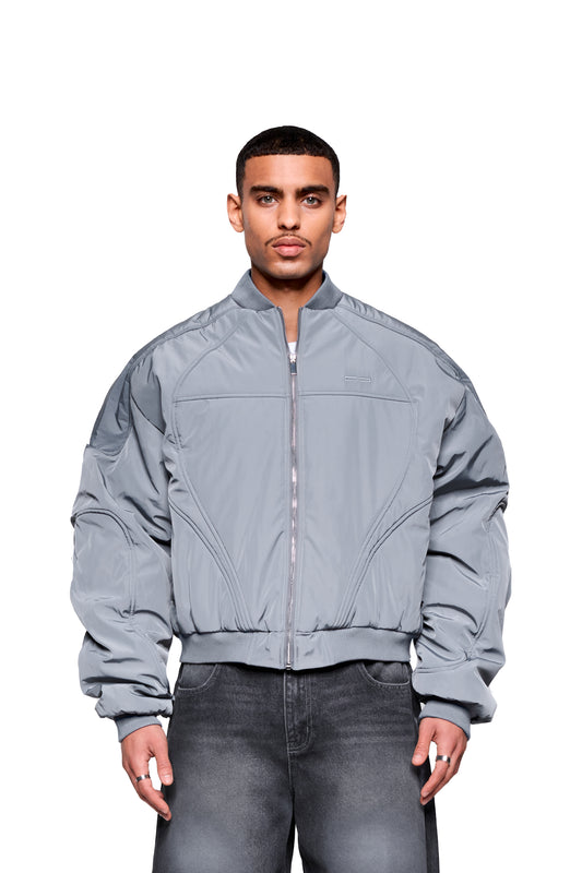 Männermodell trägt die Void Bomber Jacket Gray mit Reißverschluss, gesteppten Nähten und gerippten Details, kombiniert mit verblichenen Jeans, für eine moderne Silhouette.