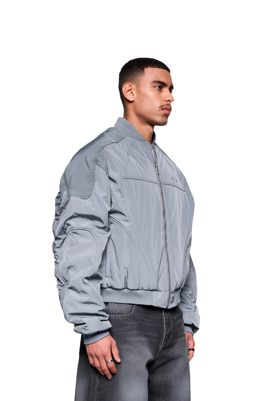 A young man seen in profile is wearing the Void Bomber Jacket Gray, featuring a zipper and ribbed cuffs, paired with gray jeans. Subtle details and a functional design.