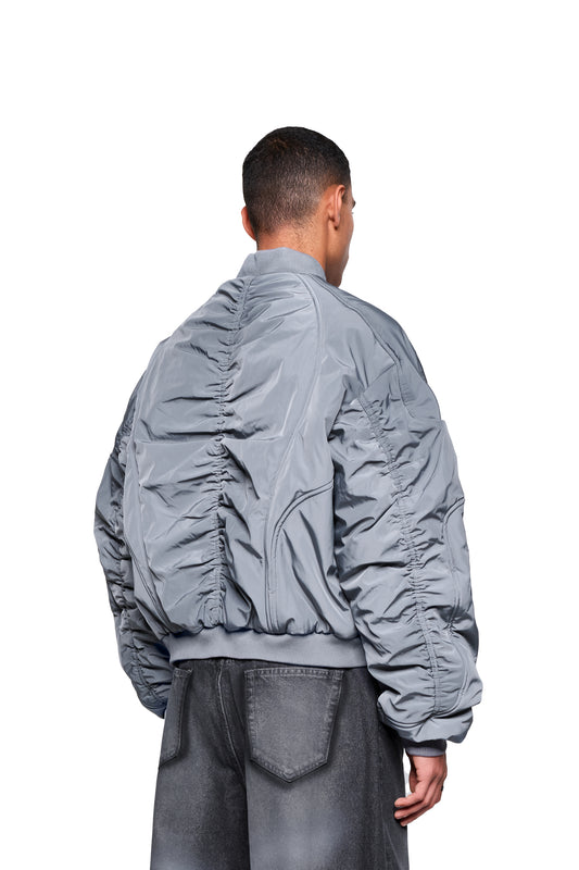 Männermodell trägt die Void Bomber Jacket Gray mit vertikalen Rüschen auf dem Rücken, kombiniert mit locker sitzenden, vintage-washed schwarzen Jeans.