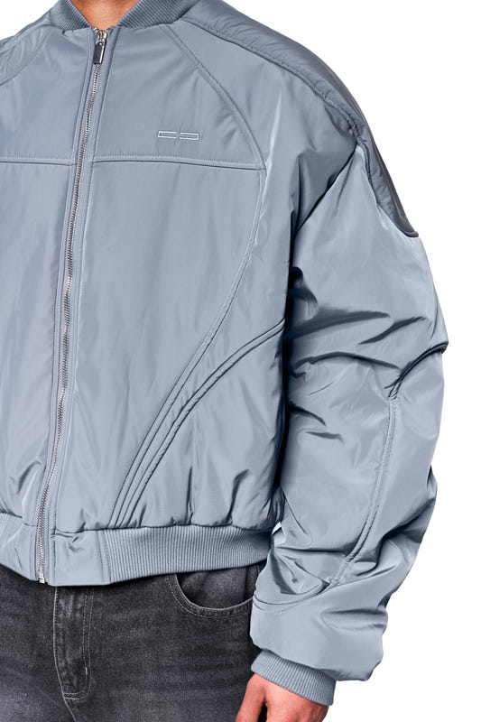 Midsection with a Void bomber jacket, slightly shiny and quilted, featuring dynamic seams and ribbed details, paired with dark jeans.