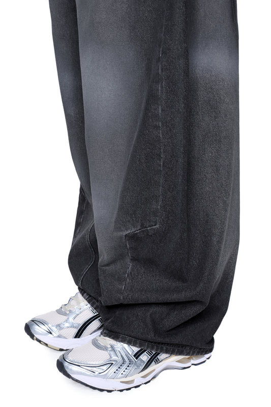 Nahaufnahme von Void Denim Pants in Baggy-Banana-Fit, die über weißen und silbernen Sneakers getragen werden. Die Hose zeigt eine Used-Optik und markante Konstruktionsmerkmale.