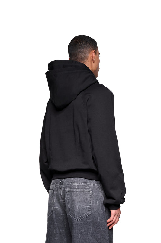 Person von hinten in einem Double Hood Hoodie Black mit Raglanärmeln, Kängurutasche und asymmetrischem Bund, kombiniert mit locker sitzenden, stone-washed grauen Jeans.