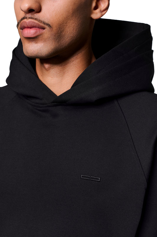 Nahaufnahme eines Gesichts mit schwarzem Double Hood Hoodie, zeigt OLAKALA Icon Stickerei auf der Brust, Kängurutasche und Raglan-Ärmel.