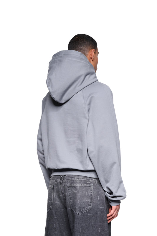 Person von hinten in einem Double Hood Hoodie Gray mit Kängurutasche und Raglanärmeln, asymmetrischem Bund und Abnäher-Detail am Rücken, trägt dunkle Jeans.