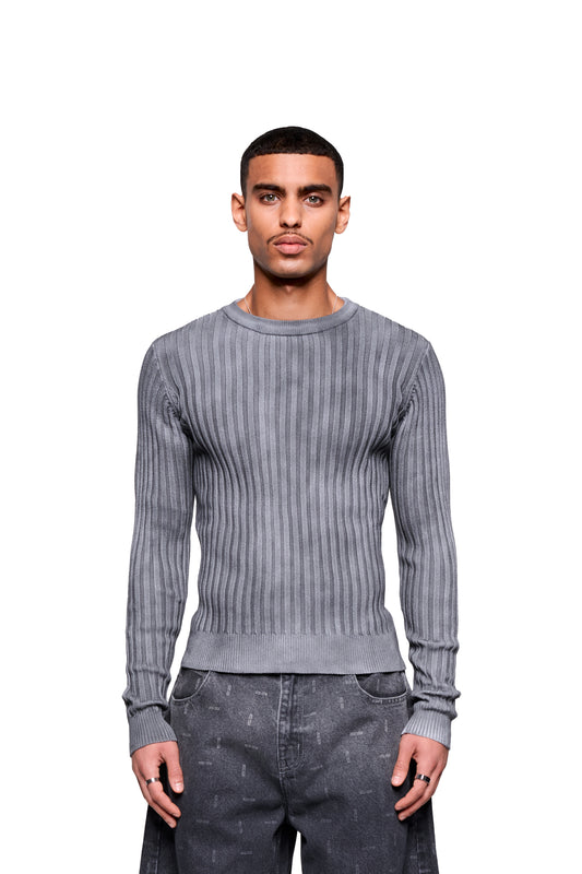 Model trägt den Void Knit Longsleeve mit Rundhalsausschnitt und besonderer Oberflächenstruktur, kombiniert mit locker sitzenden Hosen in minimalistischem Studio-Setting.