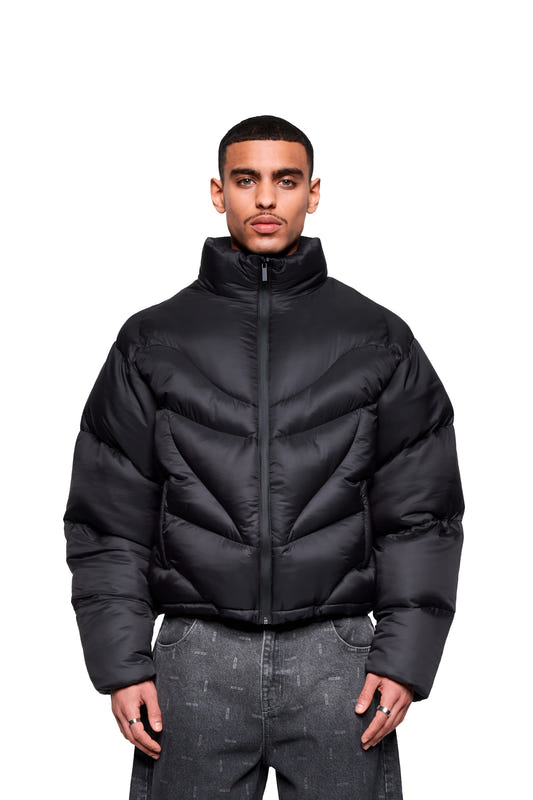 A man is wearing a Void Puffer Jacket with a chevron pattern, a high collar, and a waterproof zipper, paired with dark gray pants.
