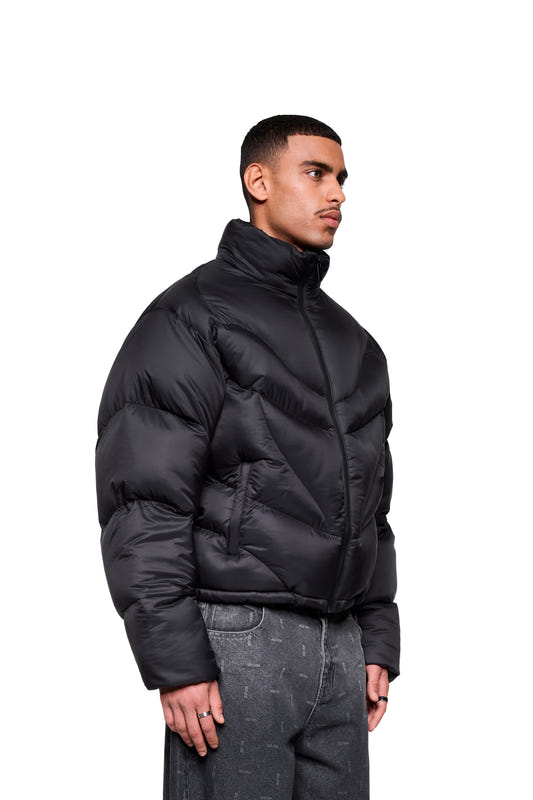 A male model, seen in profile, is wearing the Void Puffer Jacket with a high collar and a waterproof zipper, paired with loose-fitting dark gray jeans.