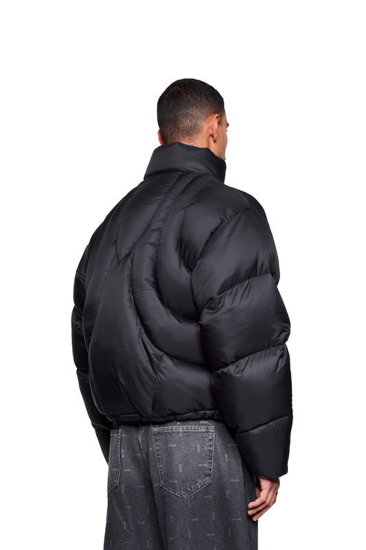 A person seen from behind wearing a Void Puffer Jacket with a high collar and quilted design, paired with loose-fitting, dark-wash jeans.