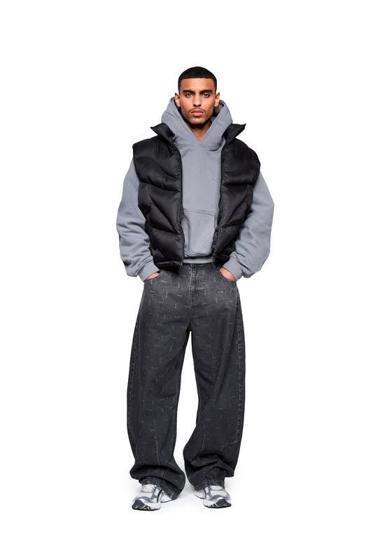 Modell trägt Void Puffer Vest über Hoodie, kombiniert mit weiten Jeans und klobigen Sneakers. Die Weste bietet eine voluminöse, anpassbare Silhouette für vielseitiges Layering.