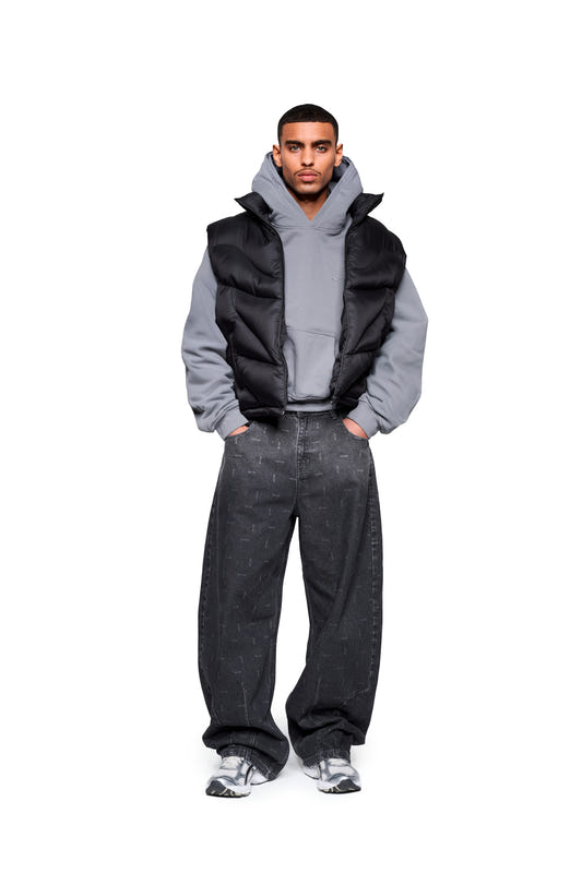 The model wears the Void Puffer Vest over a hoodie, paired with loose-fitting jeans and chunky sneakers. The vest offers a voluminous, adjustable silhouette for versatile layering.