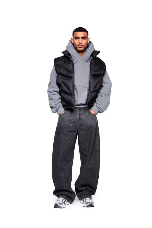 Modell trägt Void Puffer Vest über Hoodie, kombiniert mit weiten Jeans und klobigen Sneakers. Die Weste bietet eine voluminöse, anpassbare Silhouette für vielseitiges Layering.