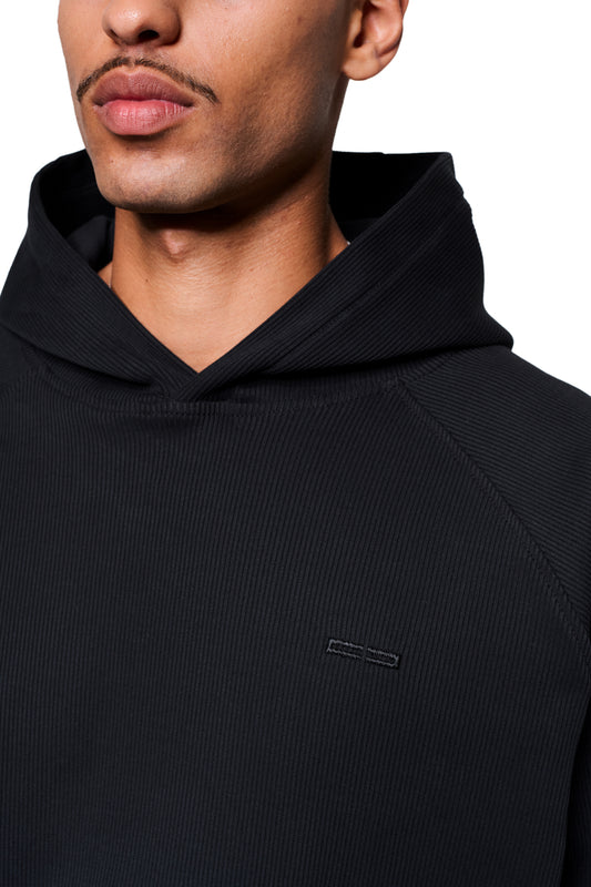 Nahaufnahme eines Mannes im Void Rib Hoodie mit feinem Rippstoff, lockerem Schnitt und Ton-in-Ton gesticktem Logo auf der Brust.