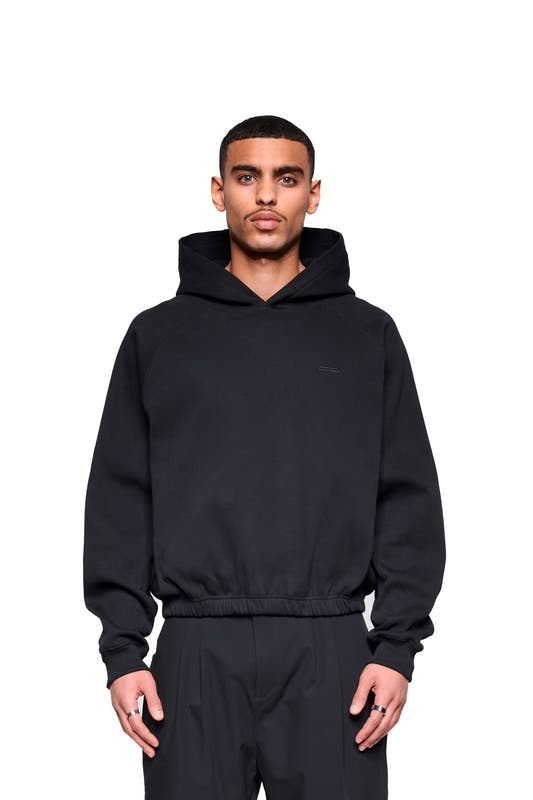 A young man wears a Void Rib Hoodie featuring a distinctive texture and boxy fit, made from sturdy ribbed fabric and designed with a raglan sleeve for a relaxed, comfortable fit.