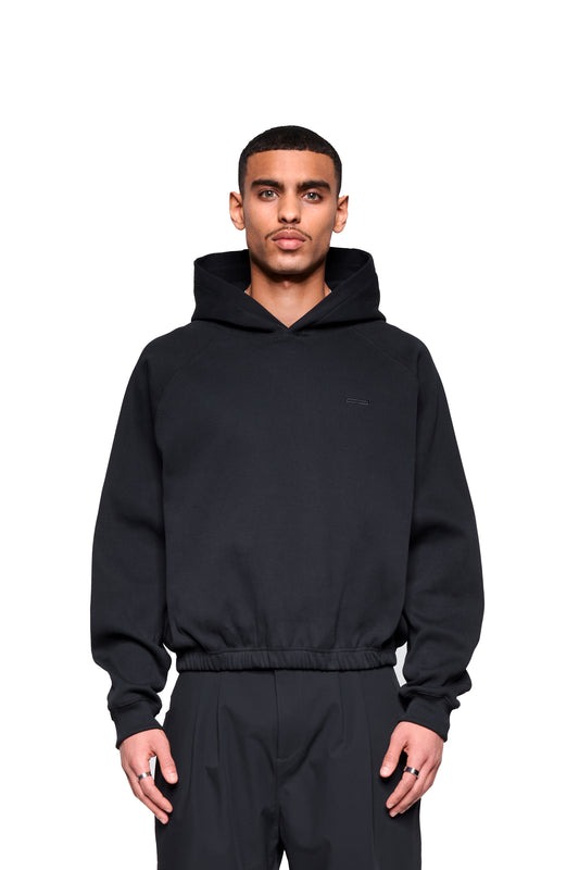 Junger Mann trägt Void Rib Hoodie mit markanter Struktur und boxy Fit, gefertigt aus festem Ripp-Bündchenstoff, kombiniert mit Raglanschnitt für entspannten Tragekomfort.
