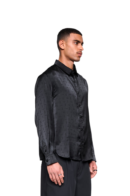 Männliches Model trägt ein Satin Shirt Black mit eingewebtem Icon-Monogramm, doppeltem Kragen und abgerundetem Saum. Lockerer Schnitt, unisex.