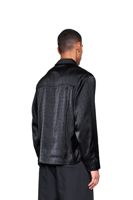 Rückansicht eines Mannes im Satin Shirt Black mit eingewebtem Icon-Monogramm, doppeltem Kragen und abgerundetem Saum, locker geschnitten, unisex.