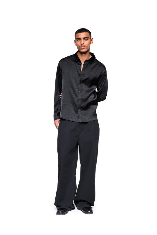 Men's black satin shirt with a woven monogram, double collar, and relaxed fit, presented in a simple fashion catalog style.