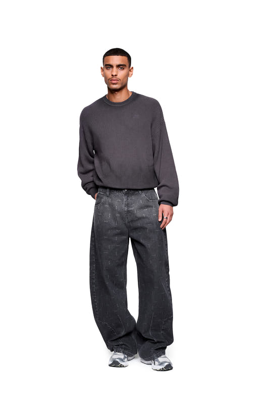 A male model wears the Void Knit Sweater in black, featuring a cropped, boxy silhouette and a distinctive texture, paired with loose-fitting dark jeans and gray sneakers.