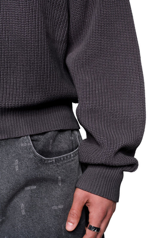 Person trägt den Void Knit Sweater Black, ein chunky-knit Pullover mit cropped, boxy Form, kombiniert mit faded-gray Jeans und schlichtem Ring am Finger.