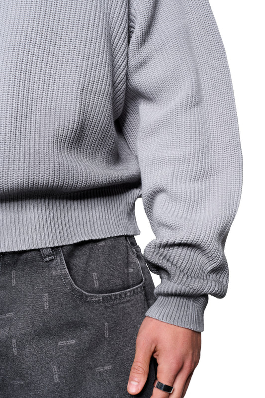 Person in grauem Void Knit Sweater und gewaschenen Jeans. Der chunky Strickpullover hat eine verkürzte, kastige Form und eine markante Struktur.
