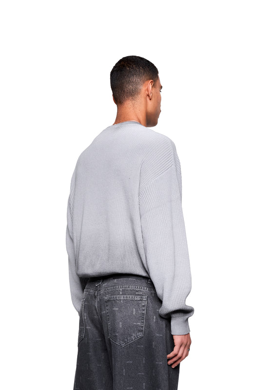 Mann trägt den Void Knit Sweater Gray mit cropped, boxy Form und markanter Strickstruktur, kombiniert mit lockeren, dunklen Jeans.