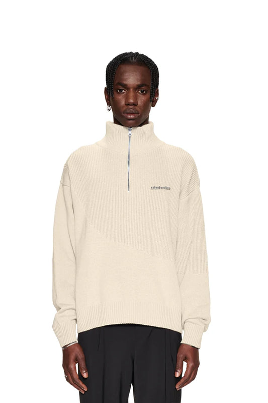 Ein Mann trägt einen weißen Strickpullover mit verschiedenen Mustern, überschnittenen Schultern und versetztem Saum, passend zur Oversized-Passform des CC Knit Halfzip Beige.