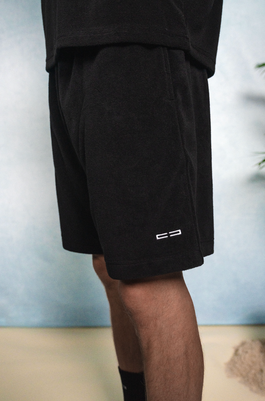 Schwarze Shorts in Seitenansicht mit kleinem weißen Logo am unteren Saum.
