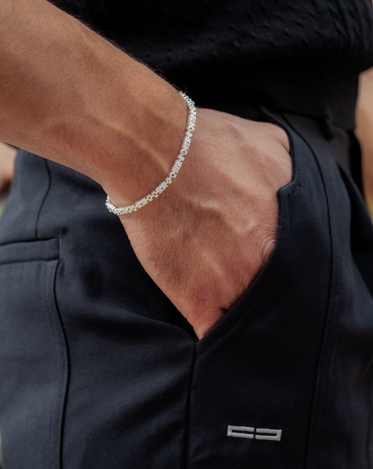Nahaufnahme: Silbernes Tennisarmband am Handgelenk eines Mannes, Hand in der Hosentasche, dunkle Kleidung.