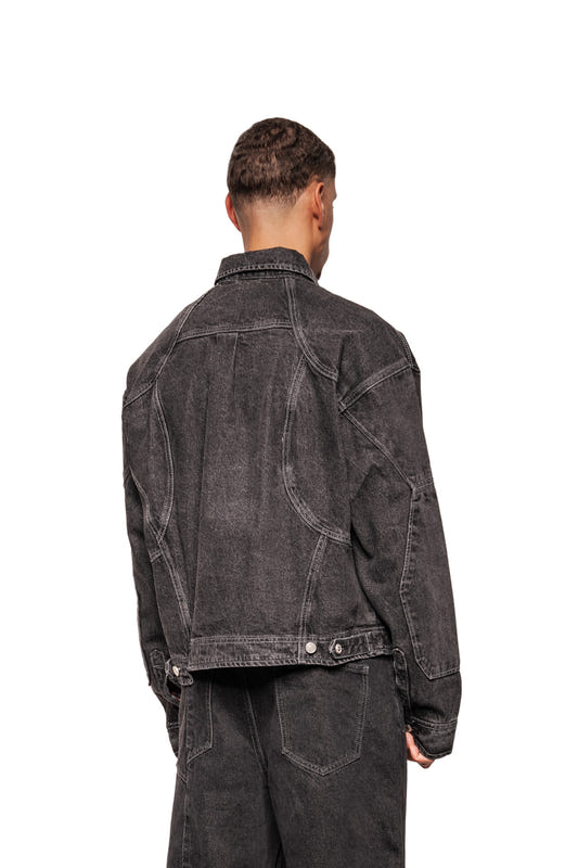 Man wears CC Black Denim Jacket with distinctive seams, breast pockets and adjustable waistband, combined with matching jeans. Oversized fit, unisex.