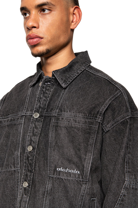 Männliches Modell trägt schwarze CC Black Denim Jacket von OLAKALA mit klassischem Kragen, Metallschnappknöpfen und gesticktem Logo auf der linken Brusttasche.