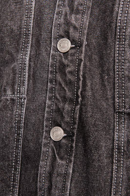 Nahaufnahme des CC Black Denim Jacket mit diagonaler Twill-Webart, sichtbaren Teilungsnähten und zwei Metallknöpfen am Frontplacket, charakteristisch für OLAKALA's Oversized Unisex-Design.