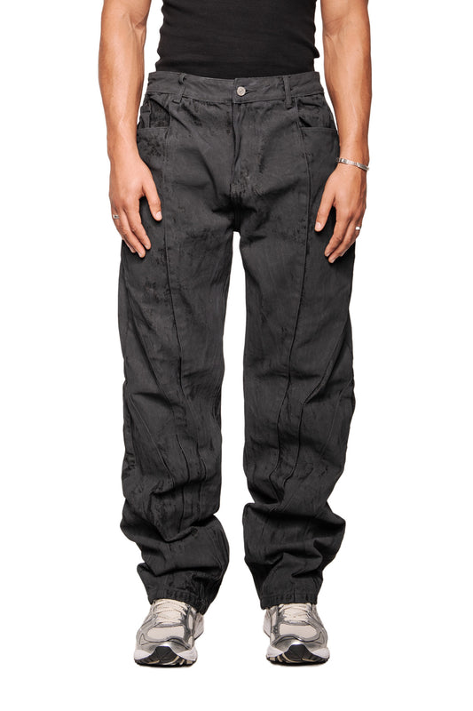 Person trägt CI Coated Denim Pants Regular mit auffälligen Nähten, Fronttaschen und silbernem Schmuck. Kombiniert mit hellgrauen Laufschuhen, betont den unisexen Stil von OLAKALA.