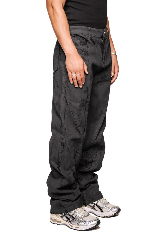 Person trägt CI Coated Denim Pants Regular mit Destroyed-Allover-Print und Teilungsnähten. Kombiniert mit silber-weißen Sneakers, Ring und Armband.