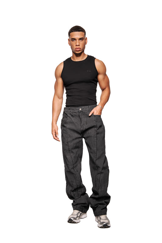 Young man in CI Coated Denim Pants Regular with visible dividing seams and 5-pocket design, matching the OLAKALA collection, looks directly into the camera.
