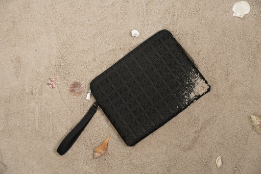 Schwarze rechteckige Grillpfanne mit Griff liegt im Sand; Muscheln liegen daneben.