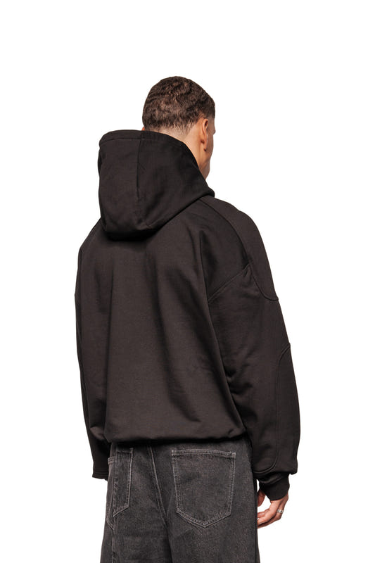 Eine Person trägt den Discreet Mask Hoodie Black mit Oversize-Schnitt, Ripp-Bündchen und gesticktem OLAKALA-Icon, kombiniert mit dunklen Jeans, Rückansicht.